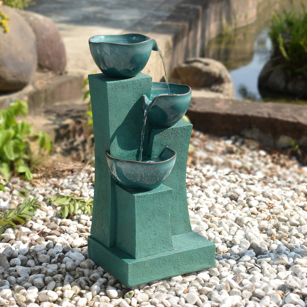 A 28.54" 3-Tier Outdoor Water Fountain with LED Lights, Green sat on white gravel next to a pond