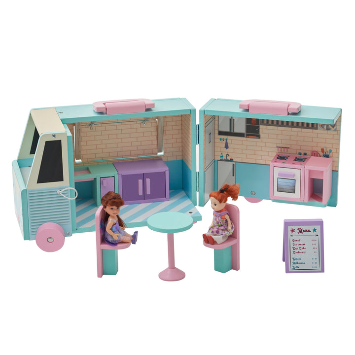 The blue and pink food truck opened with pieces inside and two dolls sitting at the table in front of the truck..