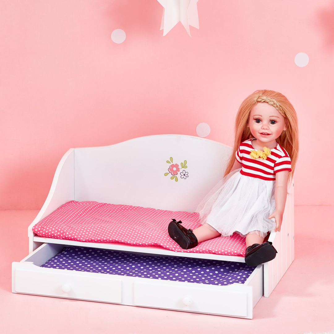 A doll dressed in a red and white striped dress sitting on the white trundle bed.