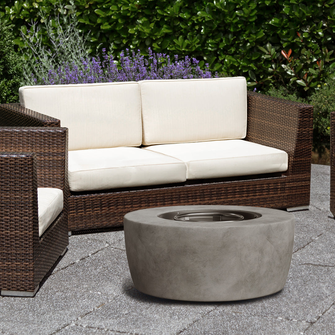 A faux concrete fire pit next to brown PE rattan furniture