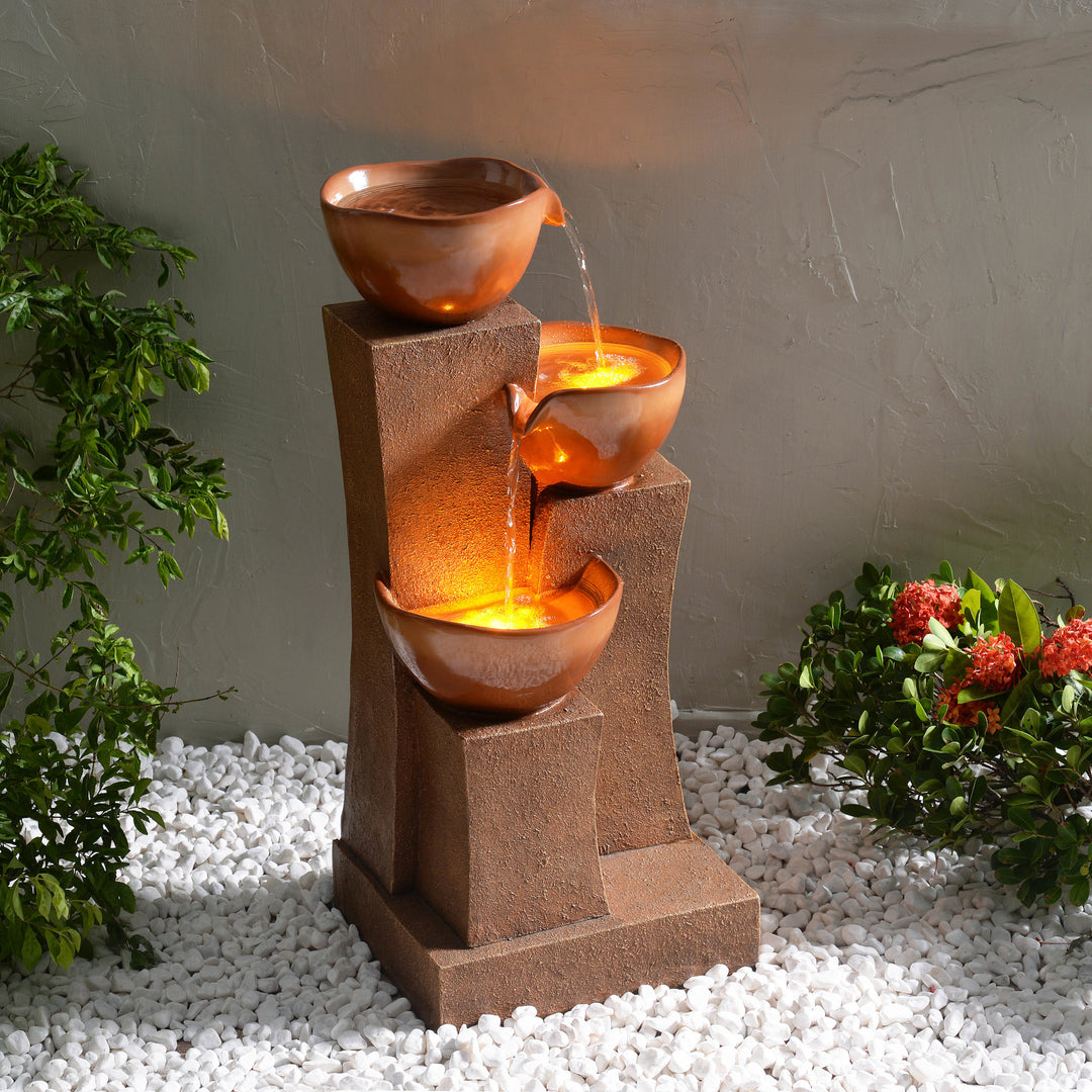28.54" 3-Tier Outdoor Water Fountain with LED Lights, Brown with flowing water set against a grey background, surrounded by plants and white pebbles.