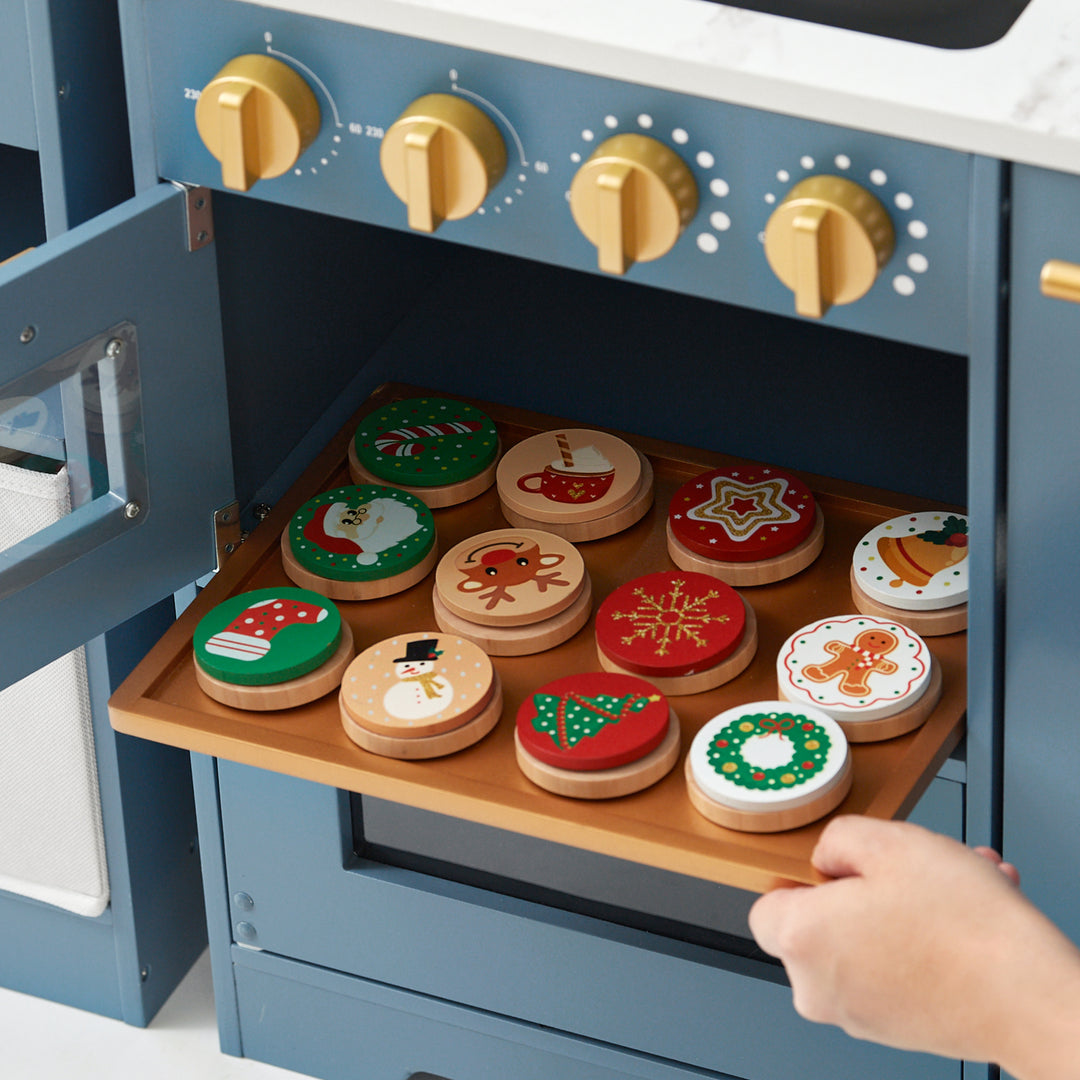 A hand opening a drawer filled with wooden toy Teamson Kids - Little Chef Atlanta Large Modular Play Kitchen, Stone Blue/Gold cookies decorated with various holiday designs.