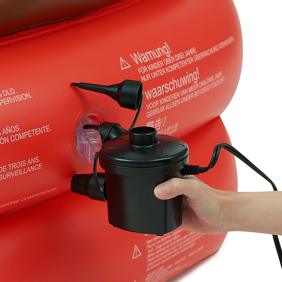A hand is operating an electric air pump attached to a Teamson Kids - Water Fun Pirate boat Inflatable Sprinkler Play with warning labels.