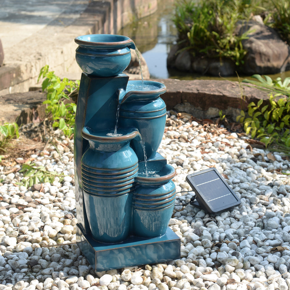 Teamson Home 28.74" Blue 4-Tier Outdoor Solar Water Fountain with LED Lights, surrounded by white pebbles with the solar panel in the sun