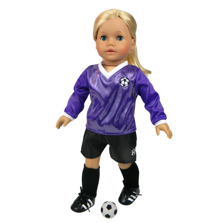 A blonde 18" Sophia's doll in a long sleeve purple soccer kit and black shorts with shin guards and cleats posed to kick a soccer ball.