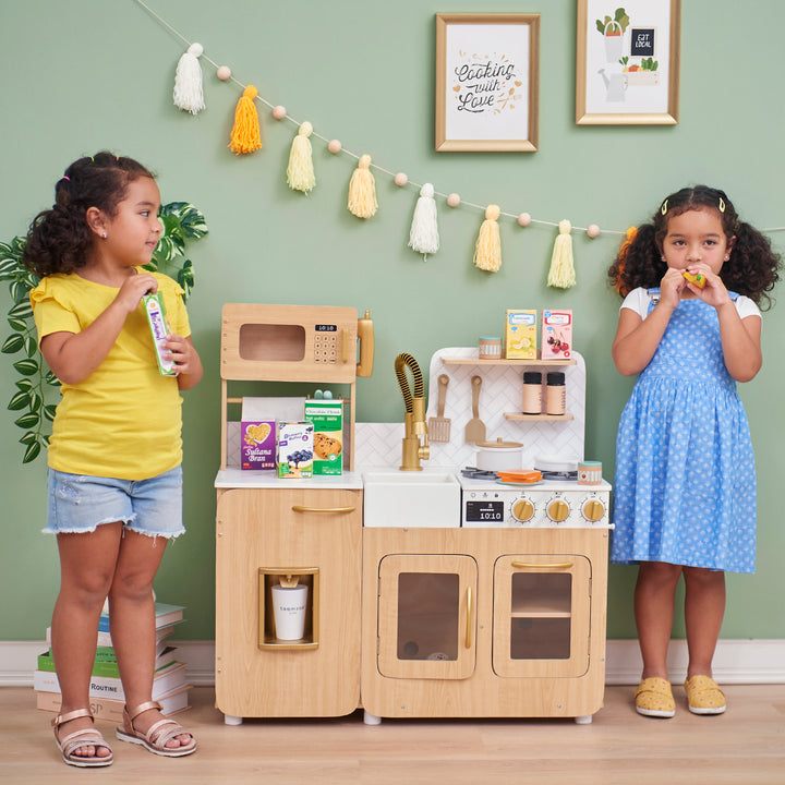 Two children playing with a Teamson Kids - Little Chef Cyprus Medium Play Kitchen, Light Oak/White.