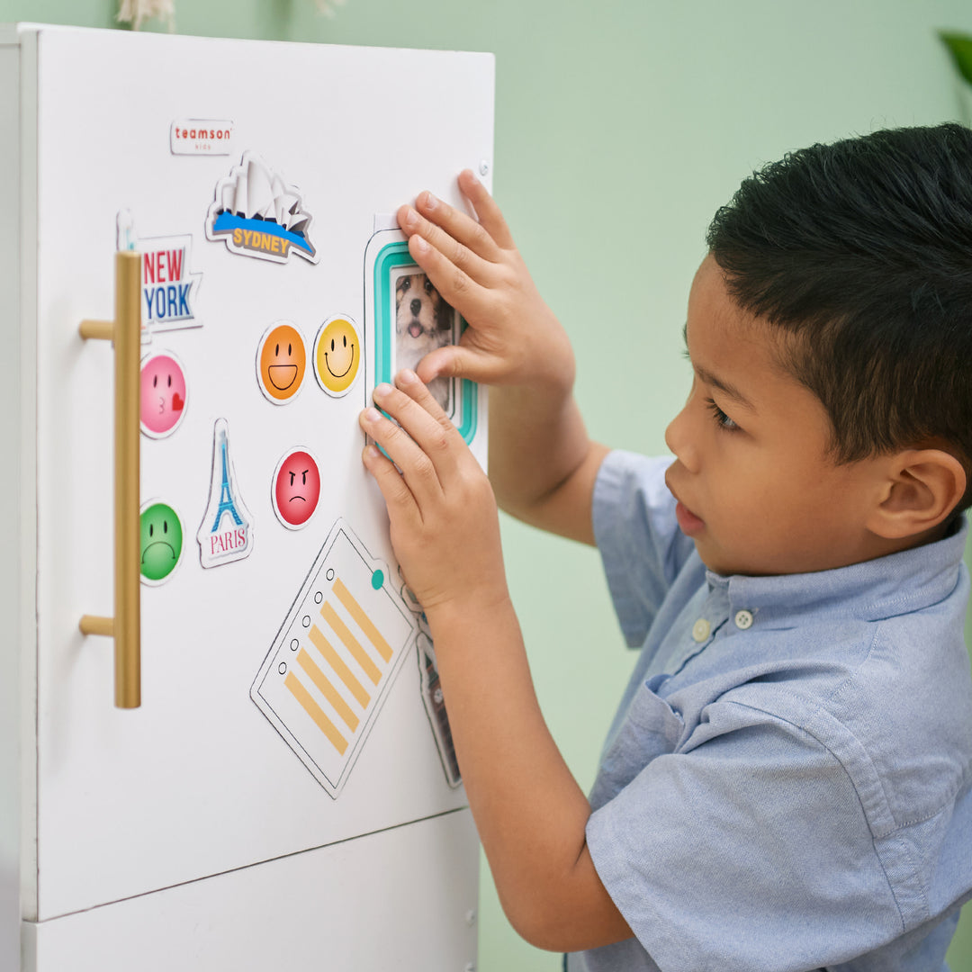 A young child playing with the TEAMSON KIDS - LITTLE CHEF ATLANTA LARGE MODULAR PLAY KITCHEN, WHITE/GOLD on a whiteboard.