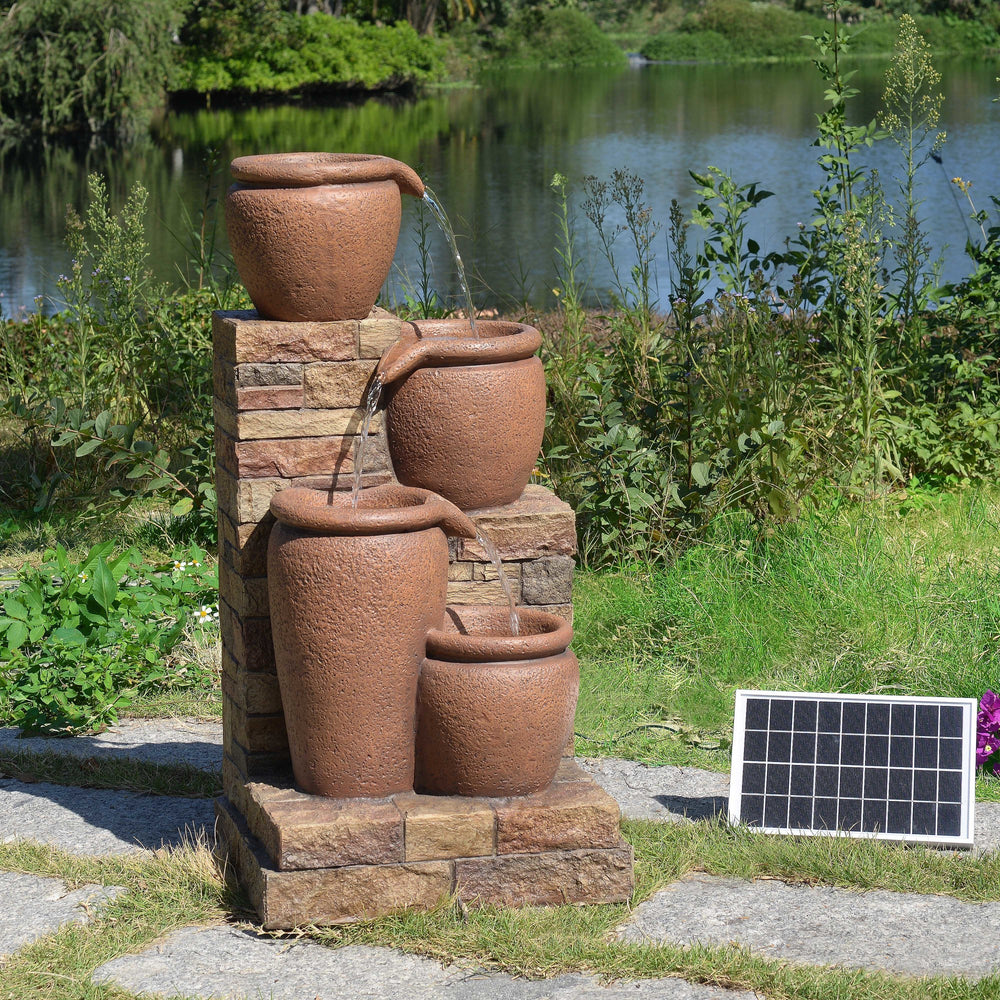 A Teamson Home 30.71" 4-Tier Outdoor Solar Water Fountain with LED Lights, Terracotta by a pond.
