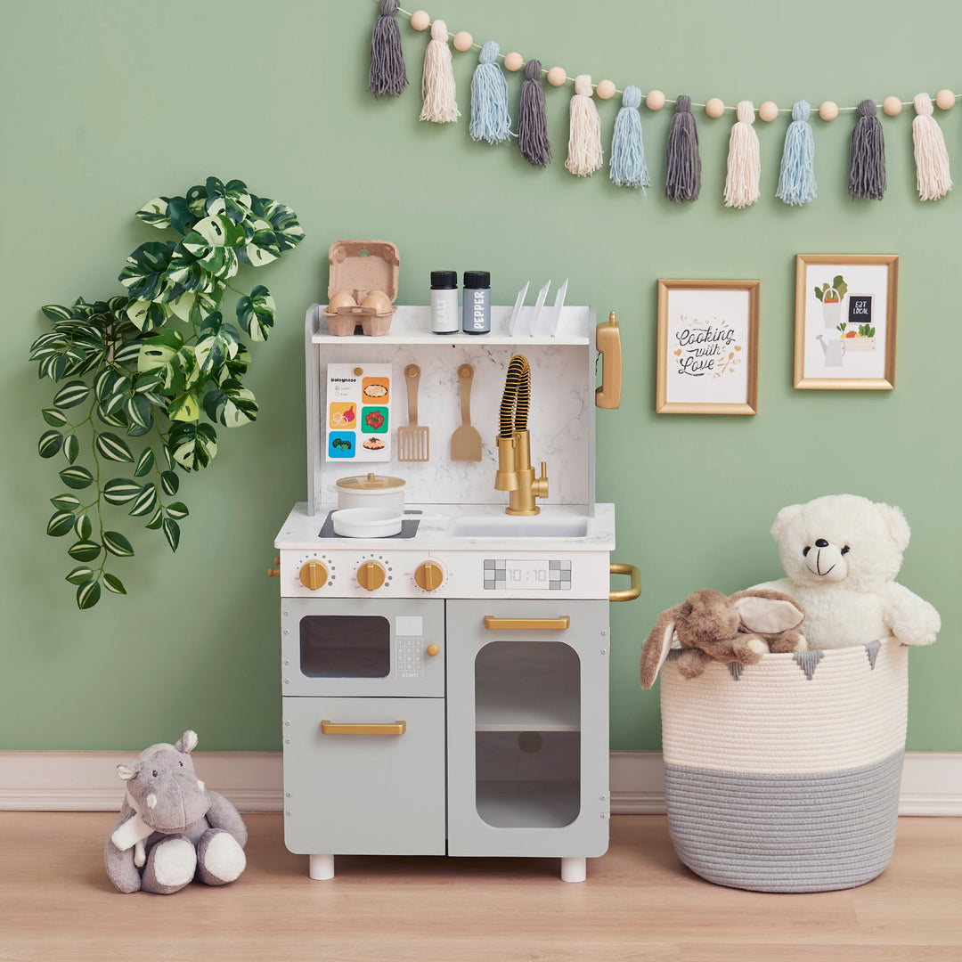 A TEAMSON KIDS - LITTLE CHEF MEMPHIS SMALL PLAY KITCHEN, GRAY/GOLD setup with toys and decorations in a room.