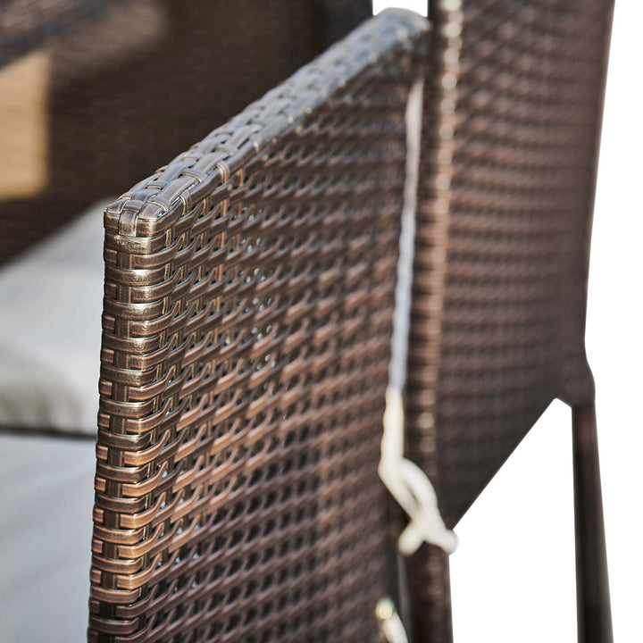 Close-up of a woven brown rattan chair from a Teamson Home 5 Pc Outdoor Wicker Dining Set with Acacia Tabletop and Cushions, with soft focus in the background.