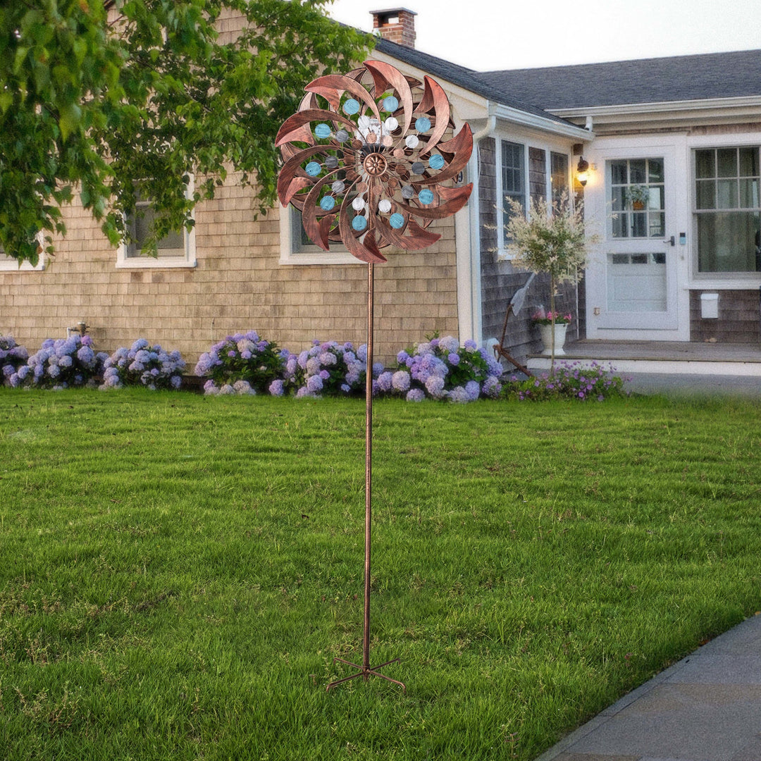 A 18" dia. x 70" H Solar Metallic Kinetic Windmill Spinner, Copper accentuates a manicured lawn in front of a residential house.