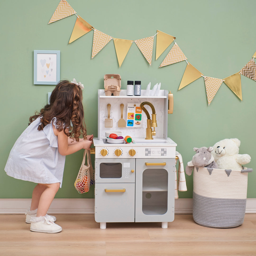 A young child playing with a Teamson Kids - Little Chef Memphis small play kitchen in a room decorated with bunting.