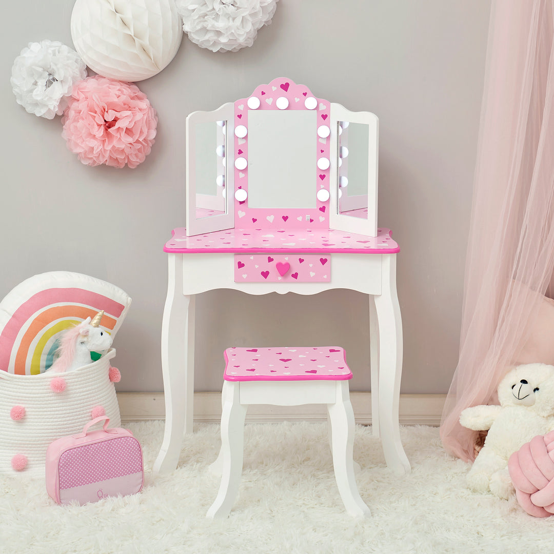 The mirror is illuminated on this white and pink vanity set with table and stool with pink heart accents and a lighted tri-fold mirror.