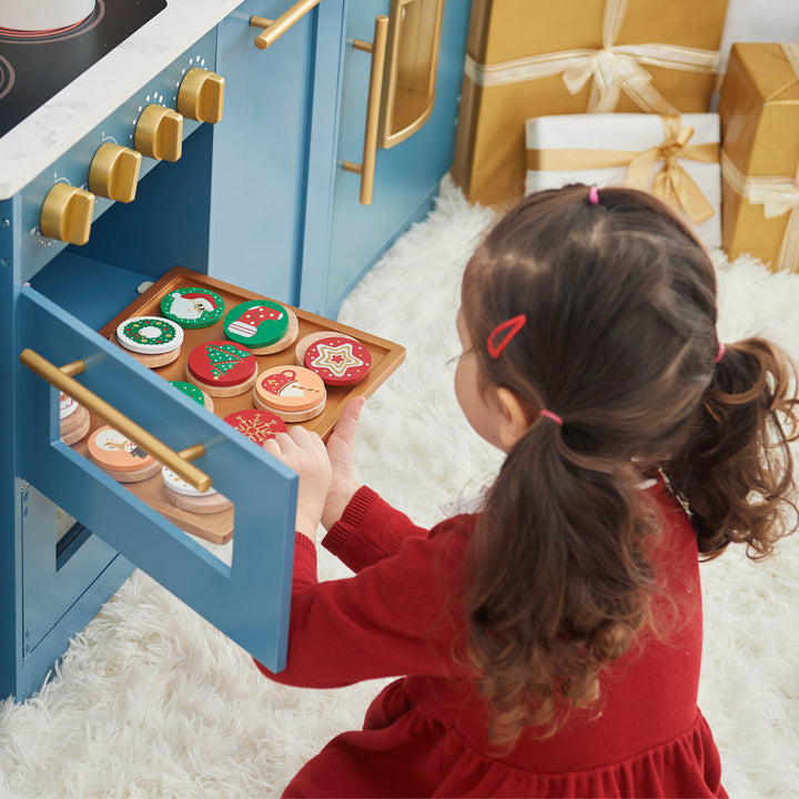 A child plays with a TEAMSON KIDS - CUTTABLE CHRISTMAS COOKIE PLAY SET and pretend cookies near a pile of wrapped gifts.