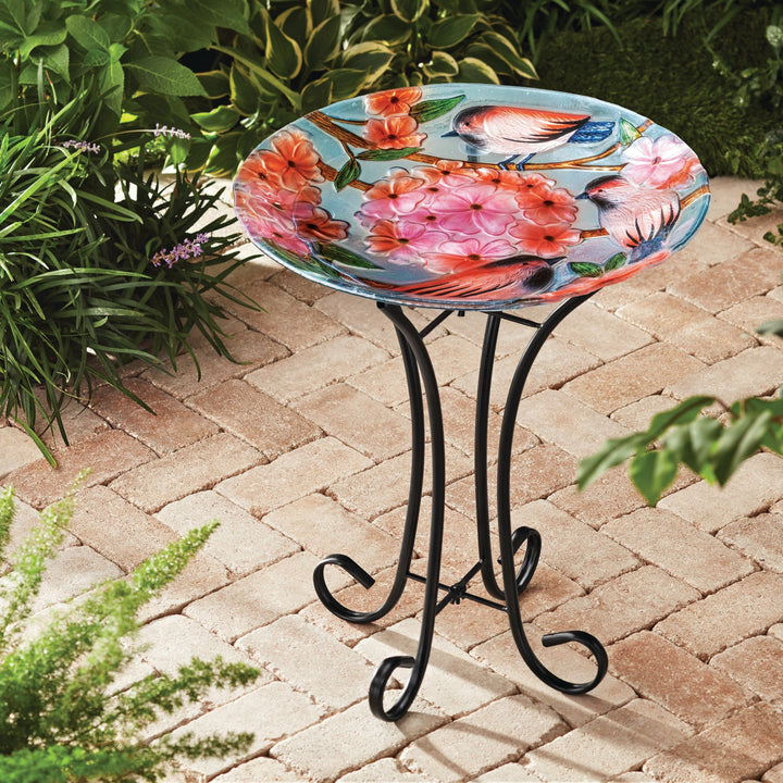 A 17.8" Robins & Blossoms Fusion Glass Birdbath with Metal Stand, Multicolored with a colorful bird on it.