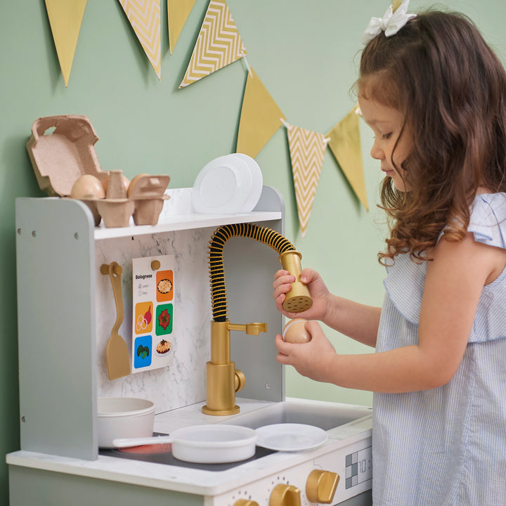 A young girl playing with a Teamson Kids - Little Chef Memphis Small Play Kitchen, Gray/Gold.