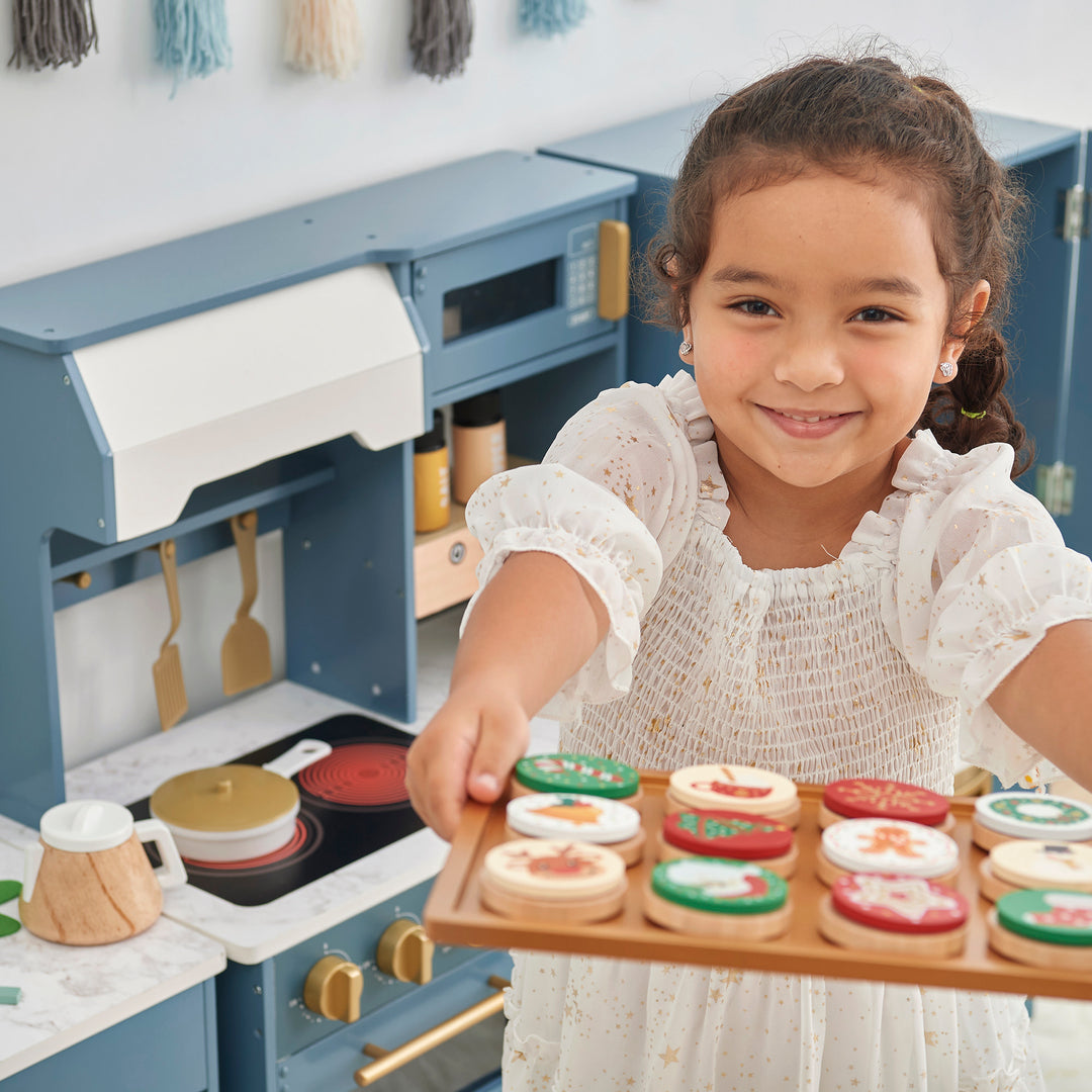 A little girl holding a tray of cookies in a Teamson Kids - Little Chef Atlanta Large Modular Play Kitchen, Stone Blue/Gold.