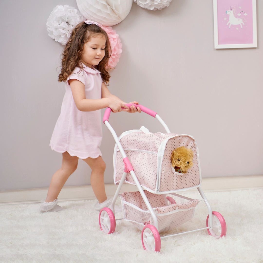 A little girl pushing around her pretend puppy in an enclosed 2-in-1 pet stroller with a detachable carrier in pink with gray polka dots.