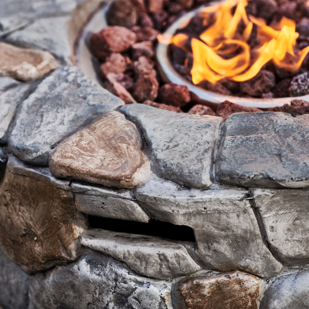 Close-up of a Teamson Home 28" Outdoor Round Stone Propane Gas Fire Pit, Stone Gray with flames and decorative lava rocks.