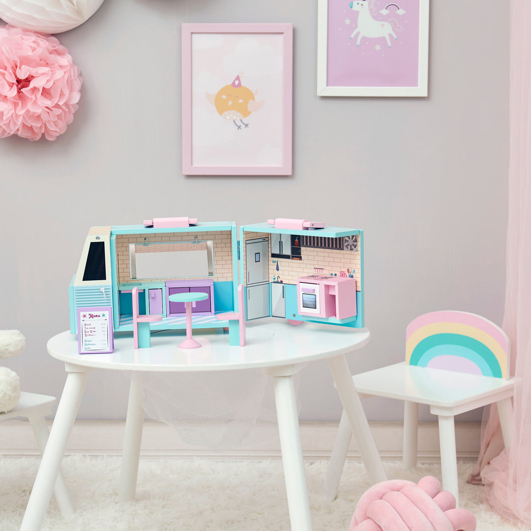 A playroom with a table, chairs, and A blue and pink food truck for dolls with a pink and white awning and accessories, opened to see the illustrated interior.