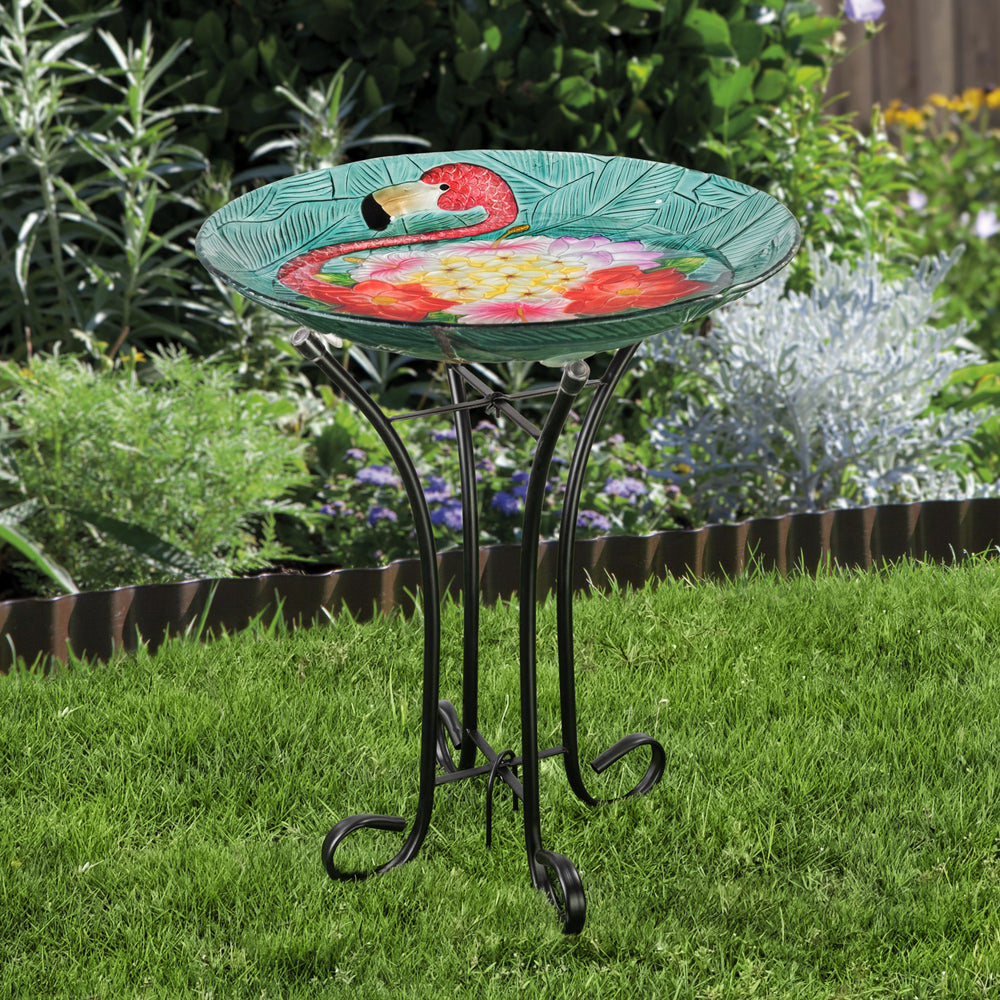 A 17.8" Fusion Glass Birdbath with A flamingo design and a Metal Stand in a garden.