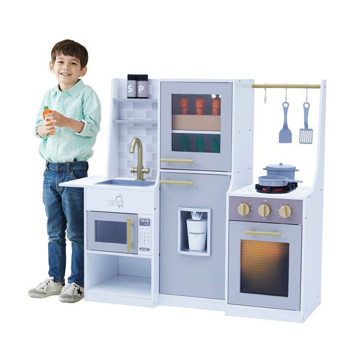 Boy smiling and standing next to the Teamson Kids Little Chef Lyon Play Kitchen.