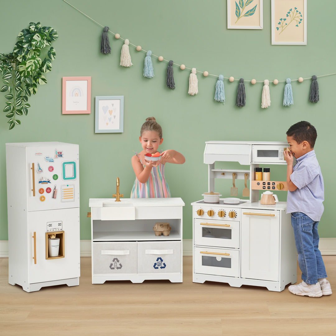 Two children playing with a Teamson Kids - Little Chef Atlanta Large Modular Play Kitchen, White/Gold.