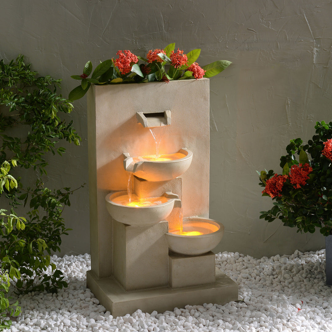 A 29.13" outdoor water fountain with planter and LED lights, surrounded by plants and white pebbles.