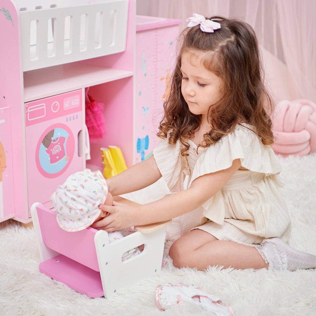 A little girl sitting her baby doll in the removable high chair from the  baby doll nursery station in pink with animal illustrations.