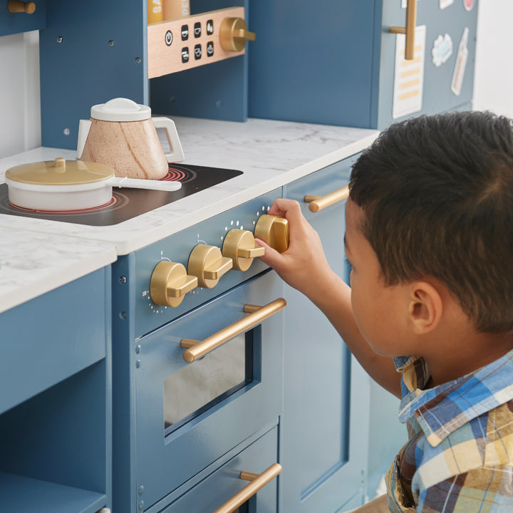 A child playing with a Teamson Kids - Little Chef Atlanta Large Modular Play Kitchen, Stone Blue/Gold.