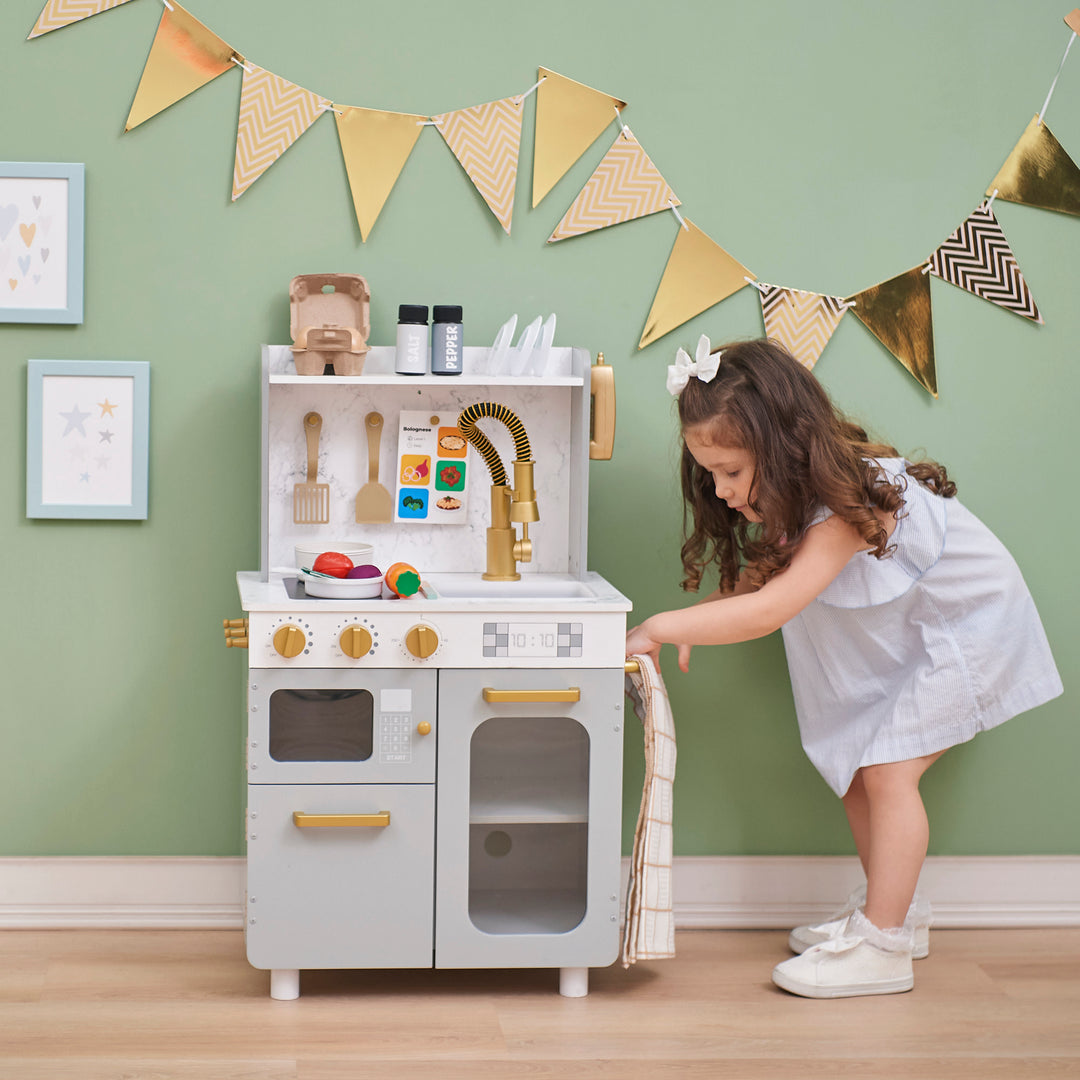 A child playing with a Teamson Kids - Little Chef Memphis Small Play Kitchen, Gray/Gold.