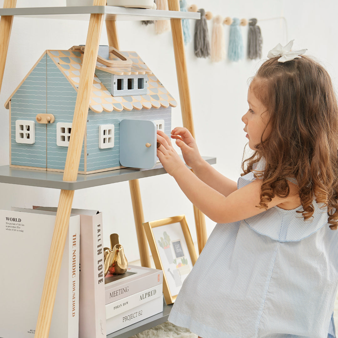 A little girl playing with Olivia's Little World - Quaint Little Cottage portable dollhouse on a shelf.