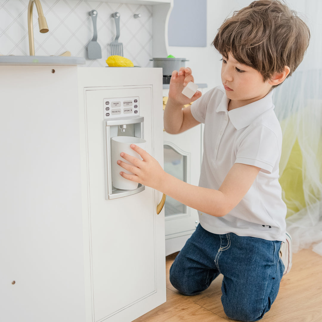 A little boy places a cup inside a pretend ice and water dispenser.