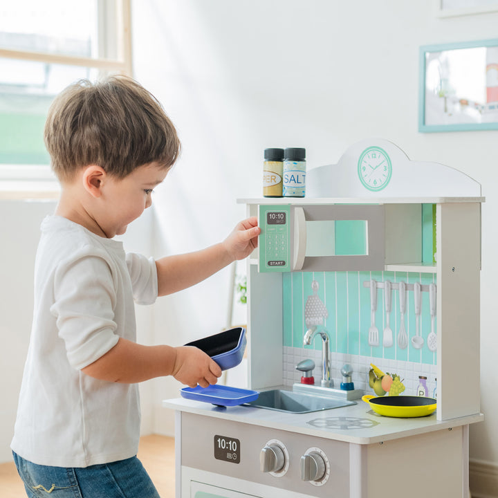 A boy opening up the microwave door of the Teamson Kids Little Chef Madrid Classic Play Kitchen with Salt & Pepper Shakers, Mint/Gray