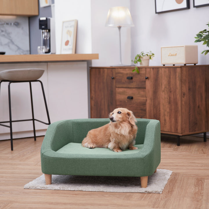 A small tan dog laying on the Bennett Linen Sofa Pet Bed for Cats and Dogs in a two-toned sea green.