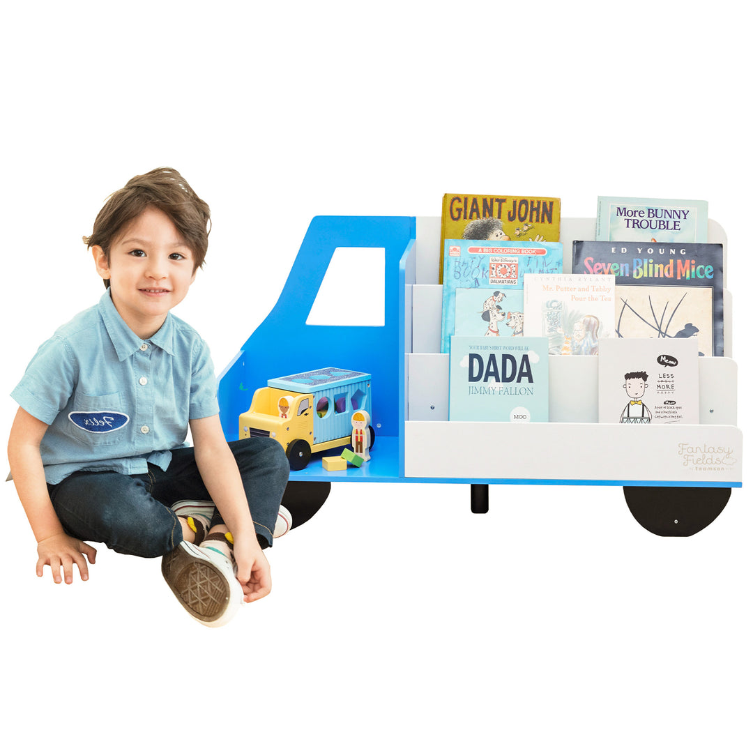 A boy sitting in front of a Fantasy Fields Truck Wooden Display Bookcase, White/Blue.
