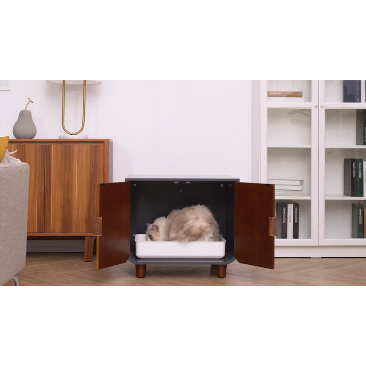 A cat napping inside a Teamson Pets Small Dyad Wooden Cat Litter Box Enclosure and Side Table, Mocha Walnut that is placed in a tidy living room with a sleek mid-century design.