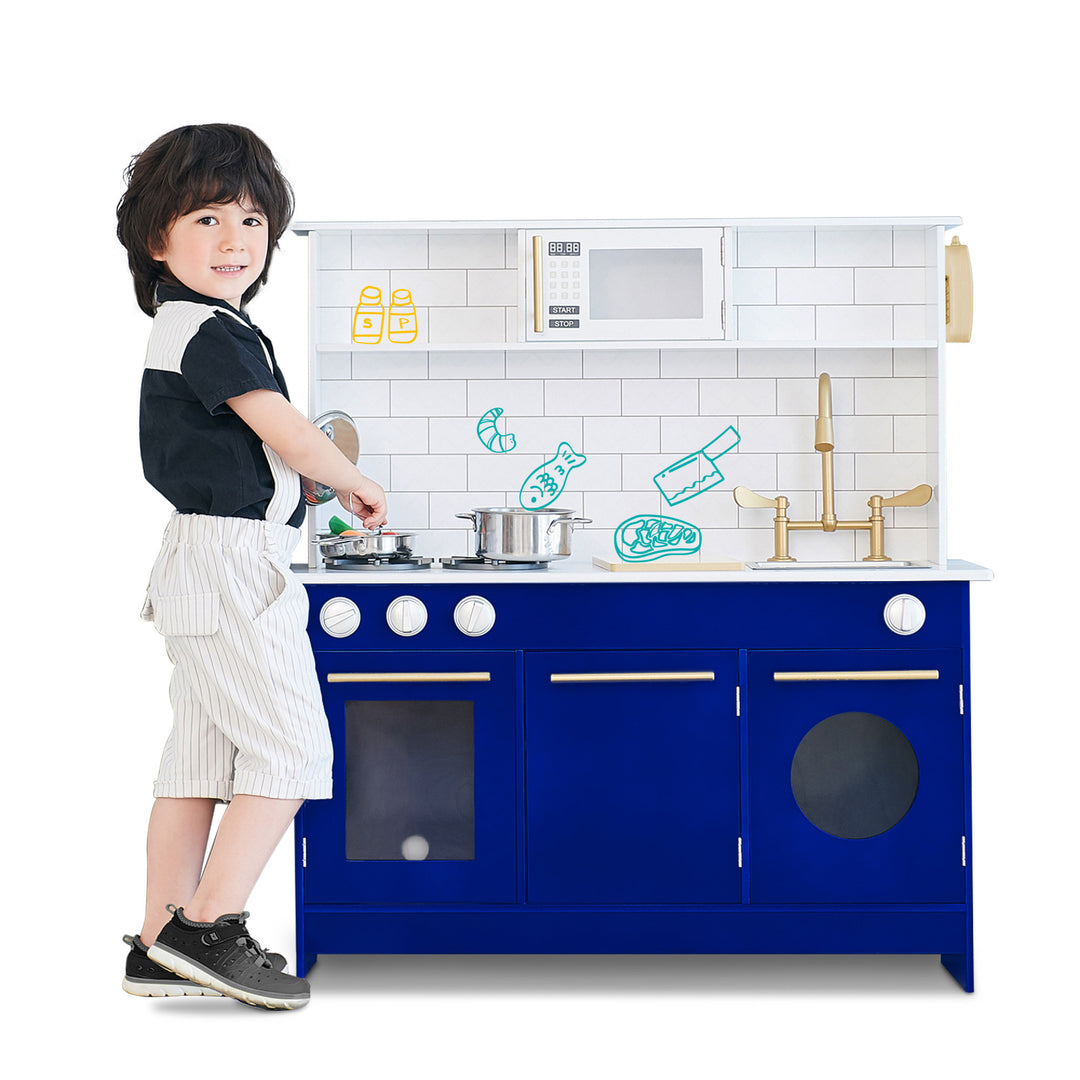 A little chef plays with a Teamson Kids Little Chef Berlin Play Kitchen with Cookware Accessories, White/Blue, pretending to cook.