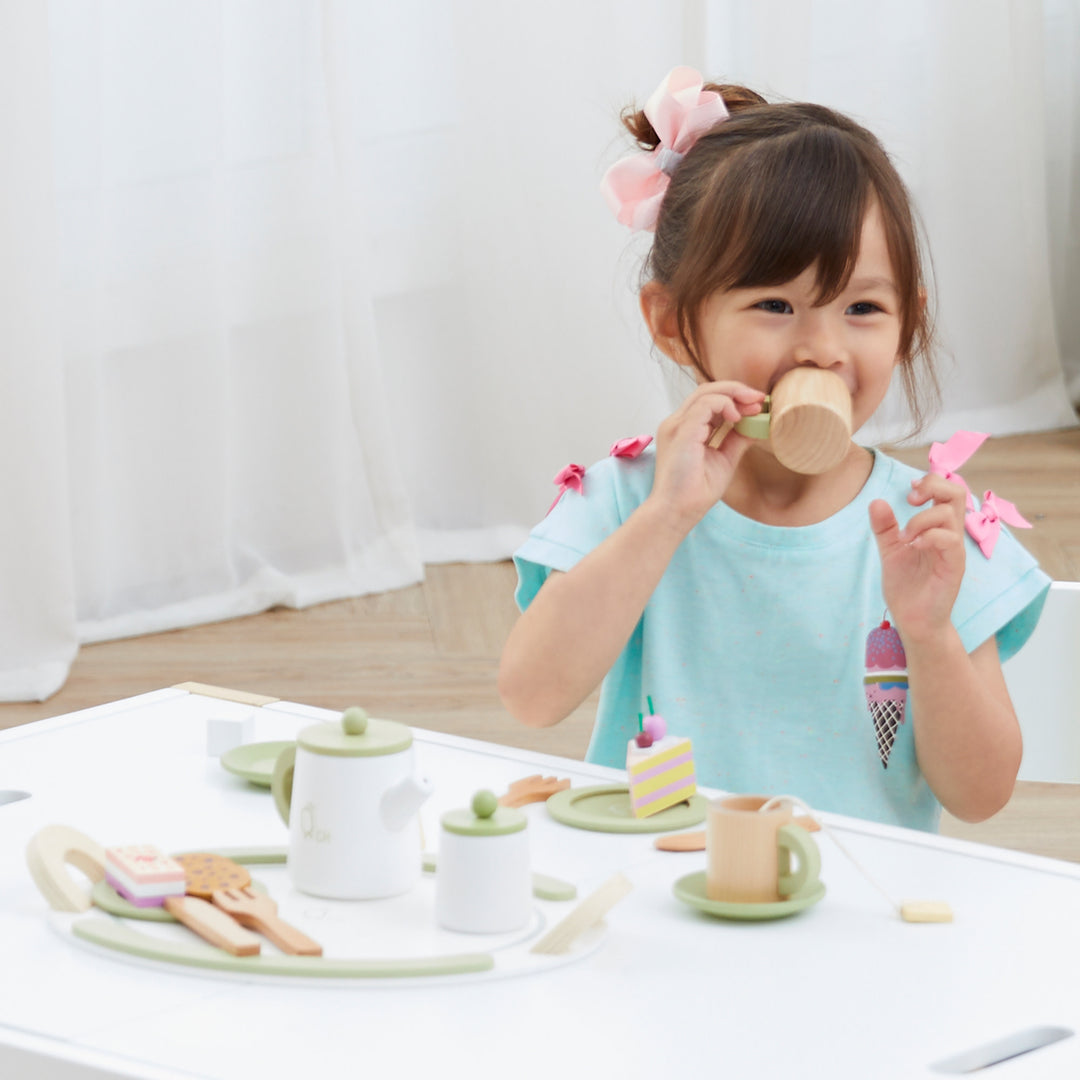 A happy child sips tea out of a wooden cup, sitting at the table with the Teamson Kids - Little Chef Frankfurt Wooden Tea sets play kitchen accessories