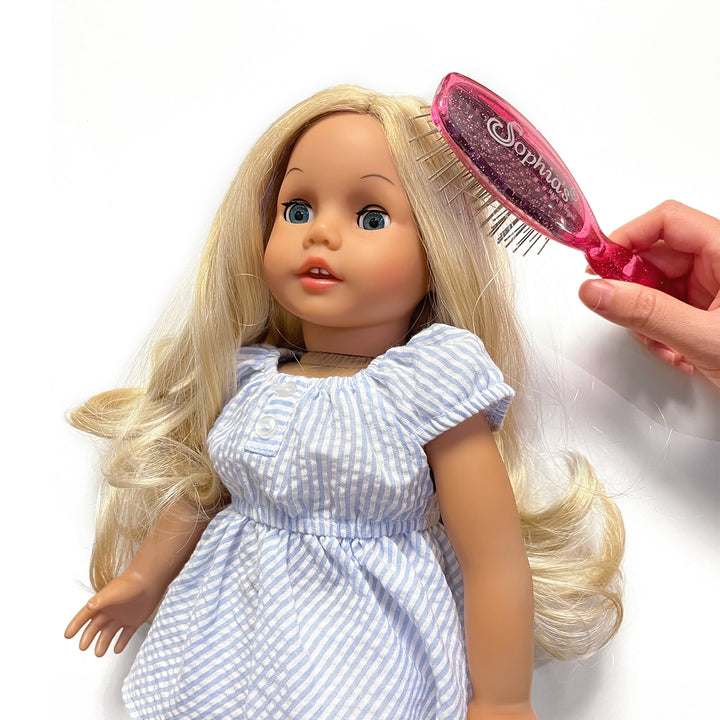 A girl is brushing the hair of a blonde Sophia's doll in a seersucker blue dress.