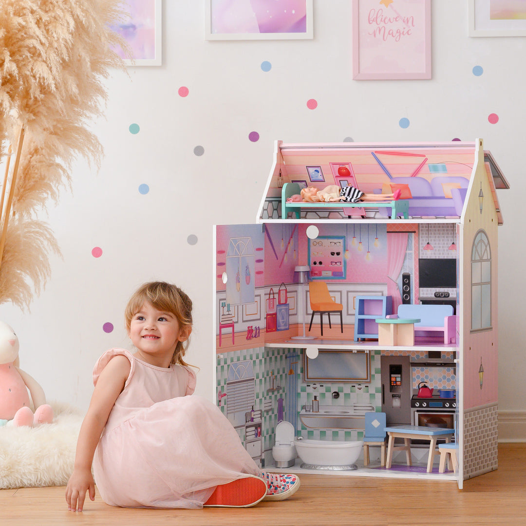 A little girl sitting on the floor in front of Olivia's Little World Dreamland Glass-Look Dollhouse for 12" Dolls with accessories.