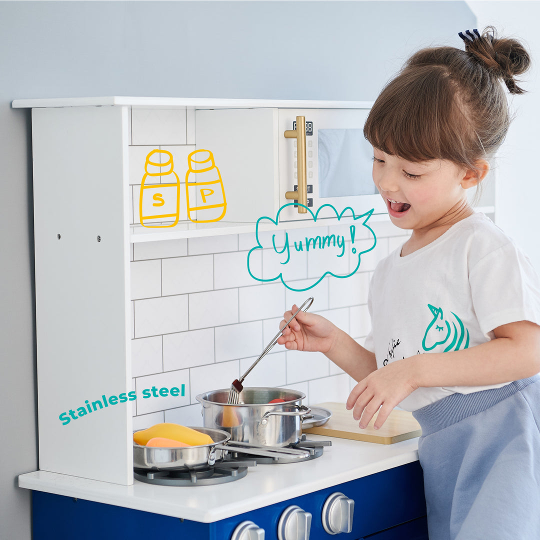 A young child happily playing with a Teamson Kids Little Chef Berlin Play Kitchen with Cookware Accessories, White/Blue, pretending to cook.