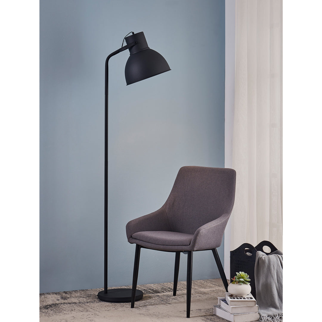 A Teamson Home Aaron 70.8" Metal Floor Lamp with Adjustable Shade, Black next to a gray chair in front of a blue wall.