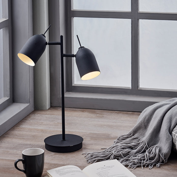 Teamson Home's Mason Modern Adjustable Double Light Table Lamp, Black next to a book and a cup of coffee.