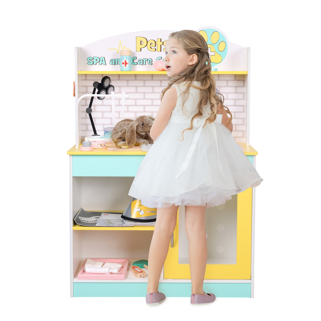 Girl in white dress stand in front of the Teamson Kids Little helper wooden pet care playset. 