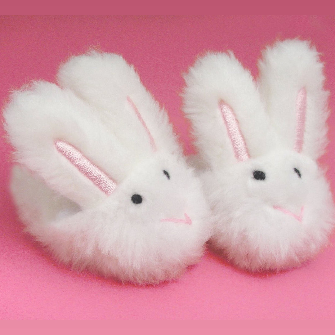 A pair of Sophia’s White Bunny Slippers with Rabbit Ears for 18" Dolls on a pink background.