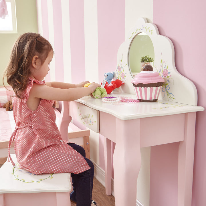 A little girl sitting on a Fantasy Fields Kids Furniture Play Vanity Table and Stool in pink and white.