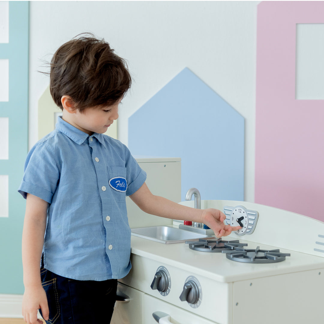 A child adjusting the knobs on an easy-to-clean Teamson Kids Little Chef Fairfield Retro Kids Kitchen Playset with Refrigerator, Ivory.