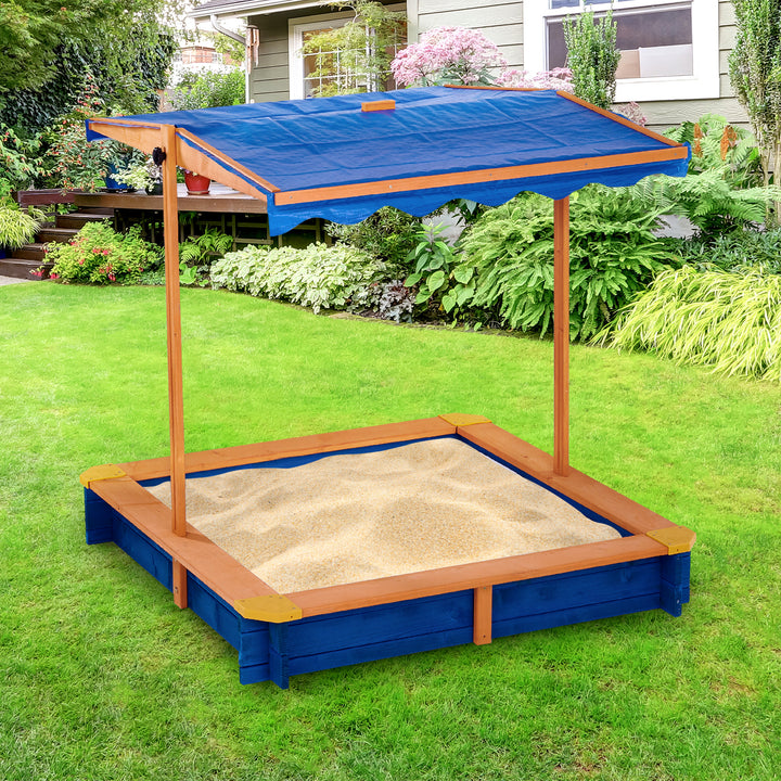 Teamson Kids 4' Square Solid Wood Sandbox with Rotatable Canopy Cover, Honey/Blue in a grassy green backyard.