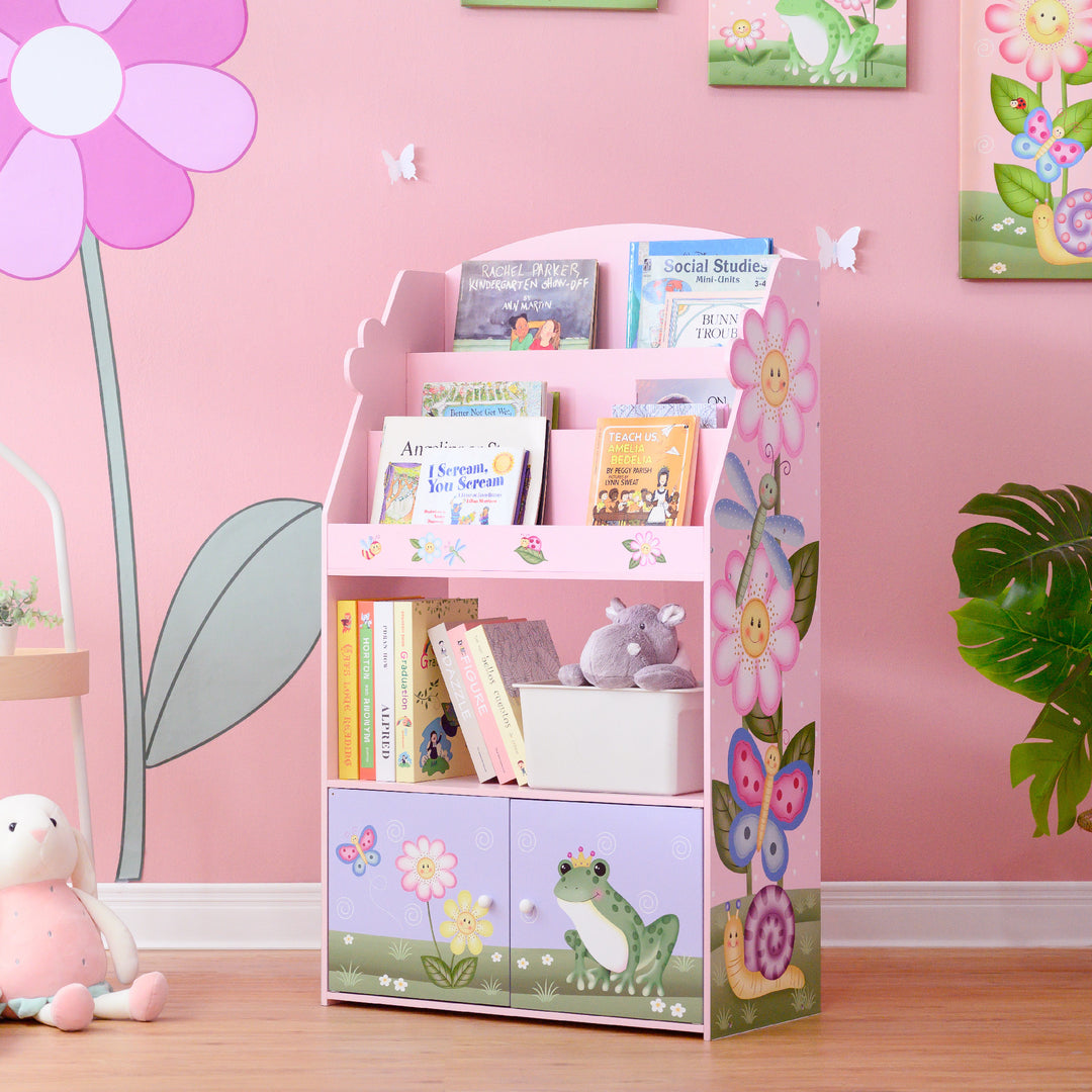 A kids' room with a pink wall and Fantasy Fields Magic Garden Kids 3-Tier Wooden Bookshelf with Storage, Multicolor.
